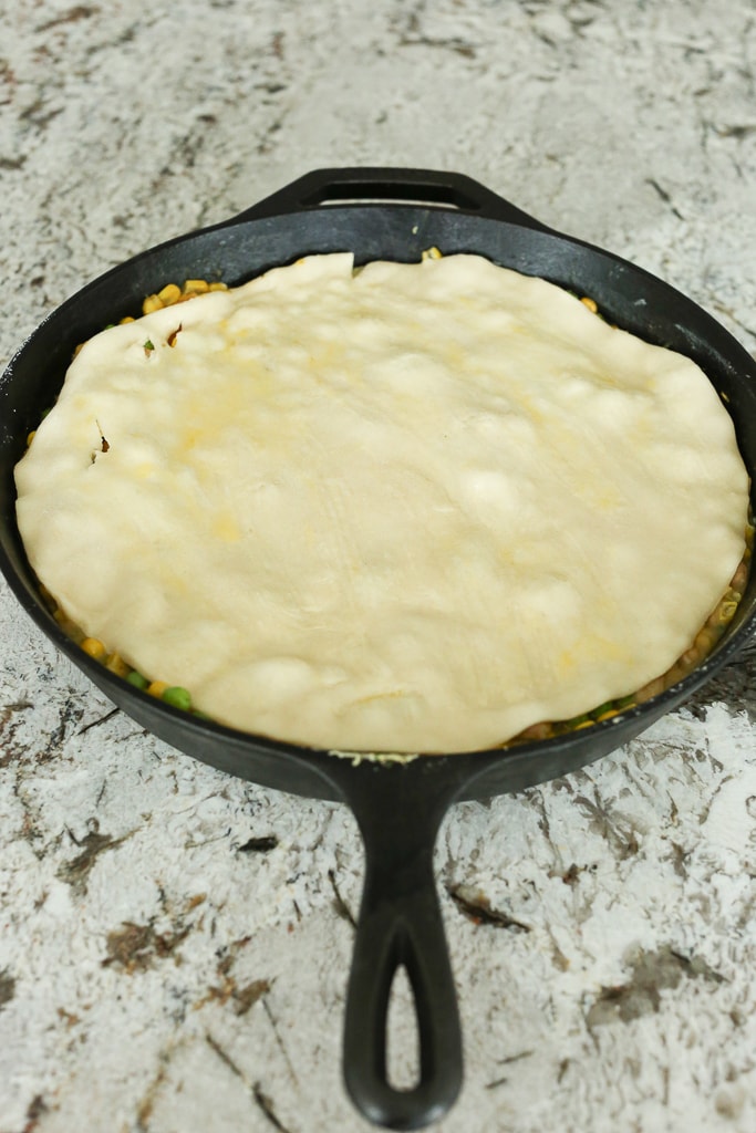 raw pie crust on top of filling in a cast iron skillet