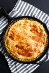 a vegetarian pot pie in a cast iron skillet with a striped napkin under the skillet