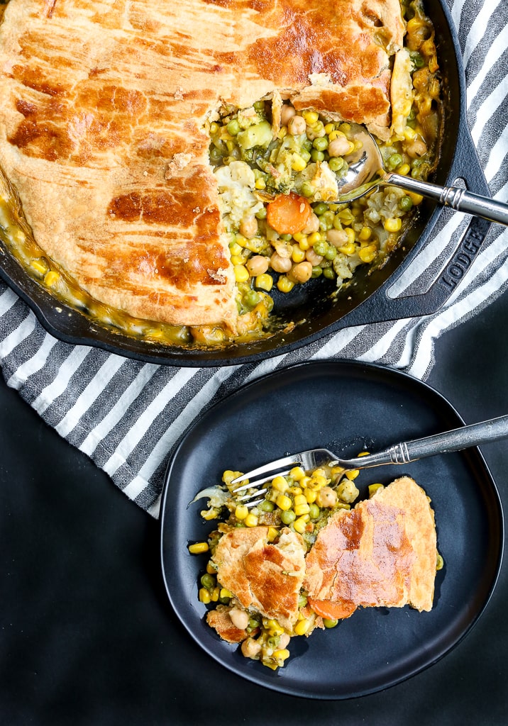 Vegetable Pot Pie Recipe showing a pie in a cast iron skillet with a piece on a plate with the vegetable filling spilling out