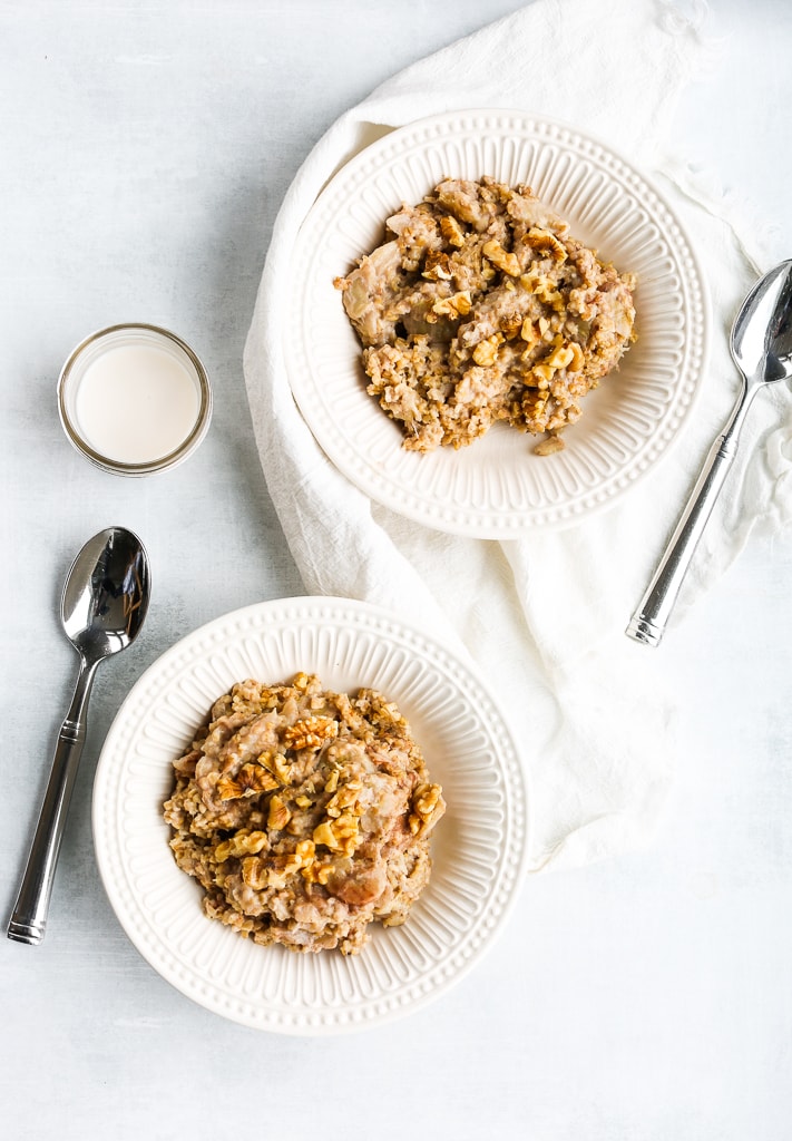 Two bowls of steel cut oats in white bowls with spoons and a white napkin