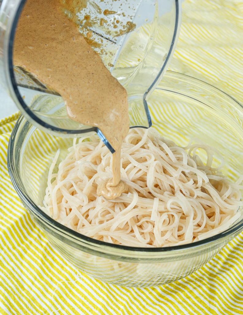 noodles in a bowl pouring sauce from a blender to the top of them 