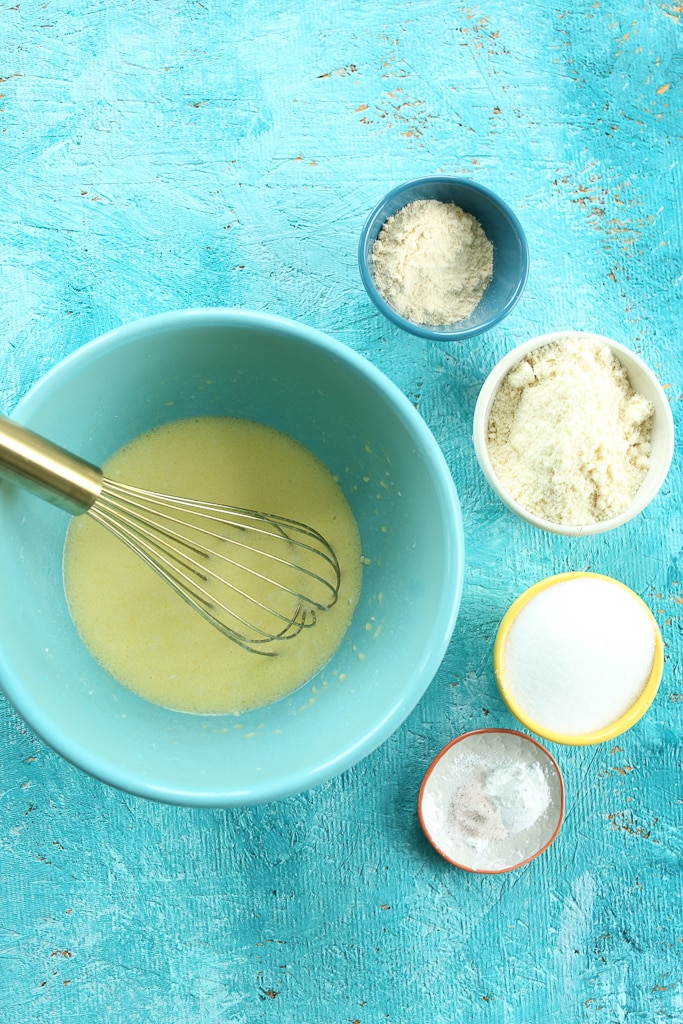 an overhead shot of wet ingredients in a turquoise bowl with a whisk, surrounded by dry ingredients in separate bowls