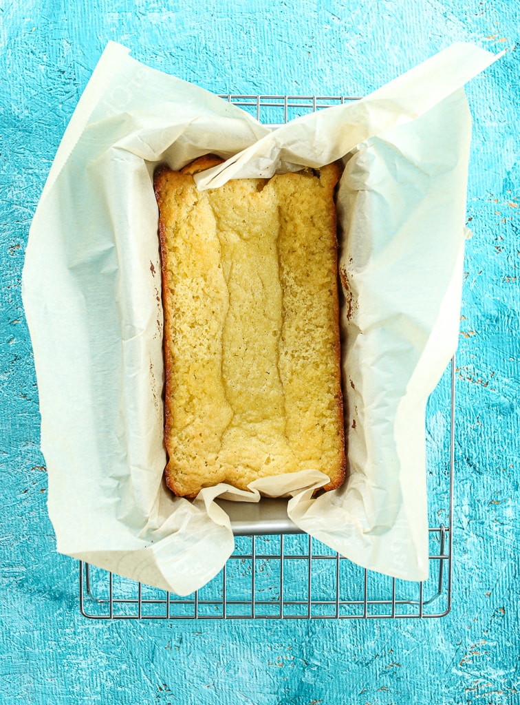 cooked cake cooling on a wire baking rack in the pan with parchment paper