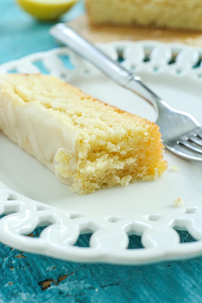 a piece of lemon loaf cake with a bite taken out on a white plate with a fork. 