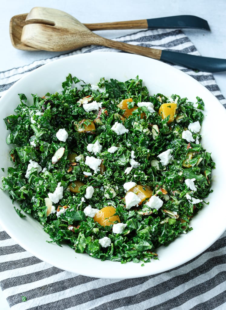 An overhead shot of the kale salad in a bowl with peaches and goat cheese and a striped napkin