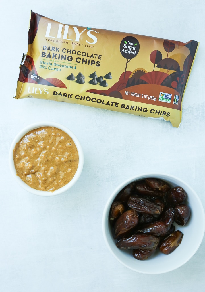 ingredients overhead shot, bag of chocolate chips, bowl of dates, and bowl of peanut butter on a white background
