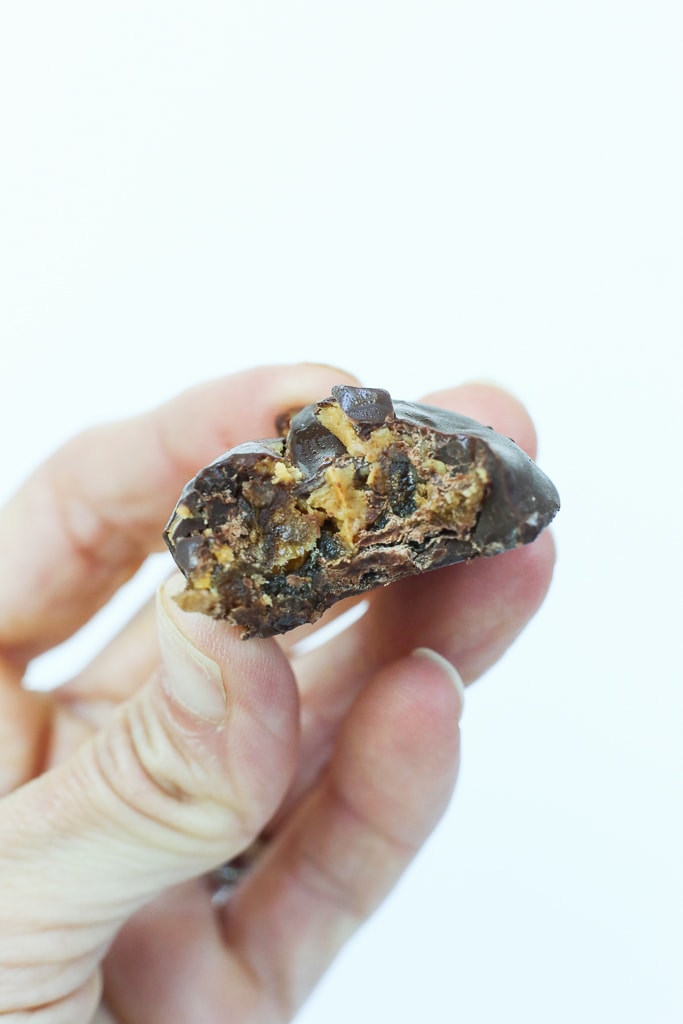 and hand holding a Chocolate Covered Peanut Butter Stuffed Date with a white background