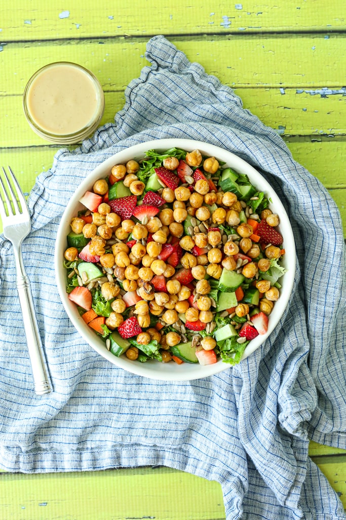 an overhead shot of a salad with lettuce, strawberry, cucumbers, and a a side of dressing 