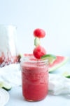 a Watermelon margarita in a mason jar with a watermelon ball and lime slice on a stick as a garnish