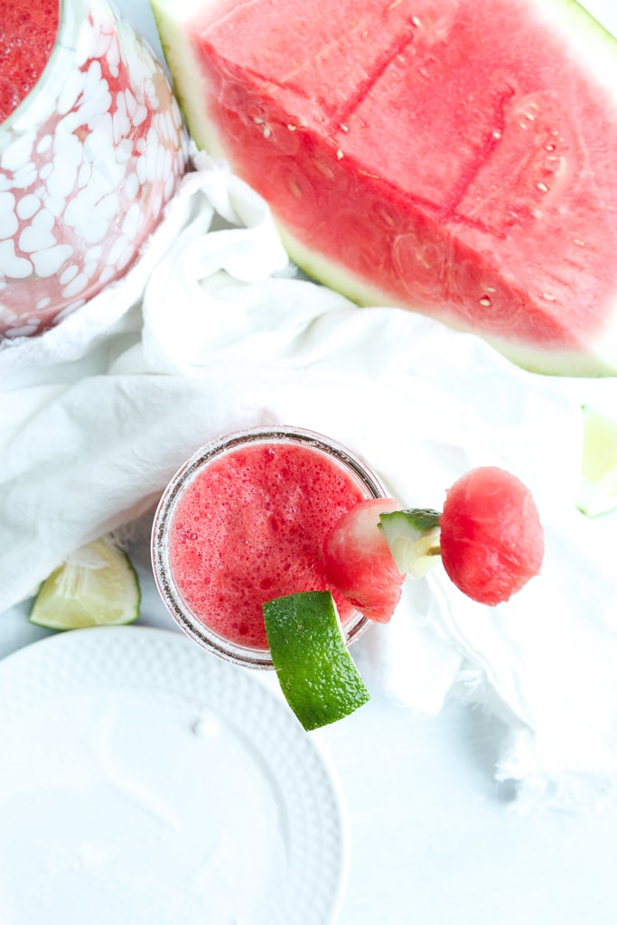 overhead shot of watermelon cocktail in a glass with a cocktail near it and a huge hunk of watermelon next to it