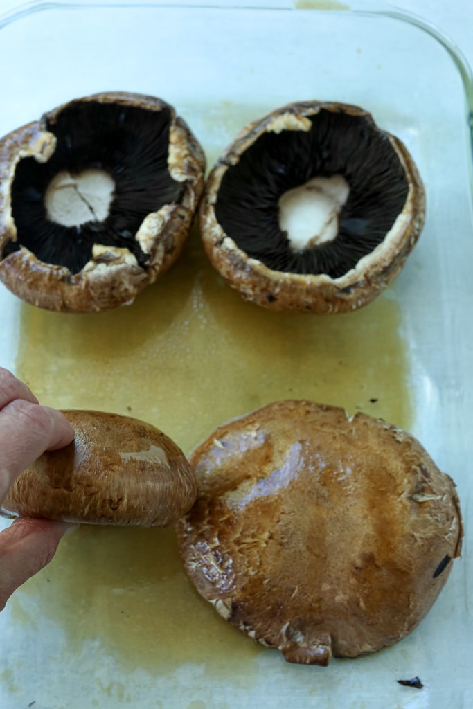 4 portobello mushroom caps in a glass shallow baking dish with marinade.