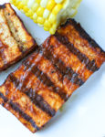 On overhead shot of grilled tofu with barbecue sauce and a little bit of corn on the cob showing on a white plate