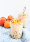 2 mason jars filled with overnight oats topped with peaches and almonds on a blue and white striped napkin and fresh peaches in the background