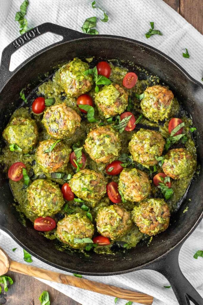 overhead shot of chicken meatballs in a pesto sauce in a black pan