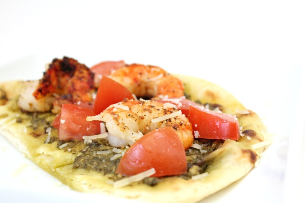 a flat bread with pesto shrimp and tomatoes