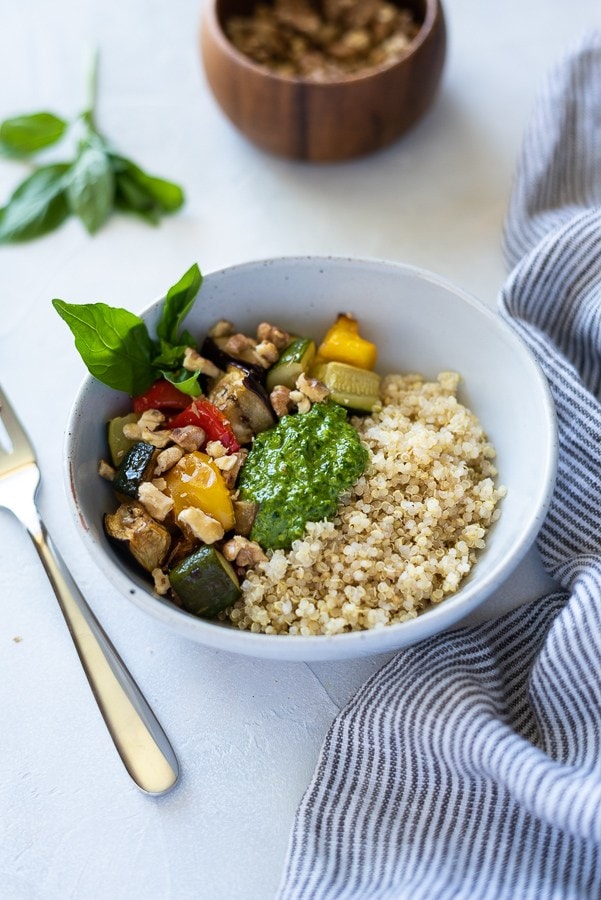 a white bowl with vegetables, quinoa, and pesto