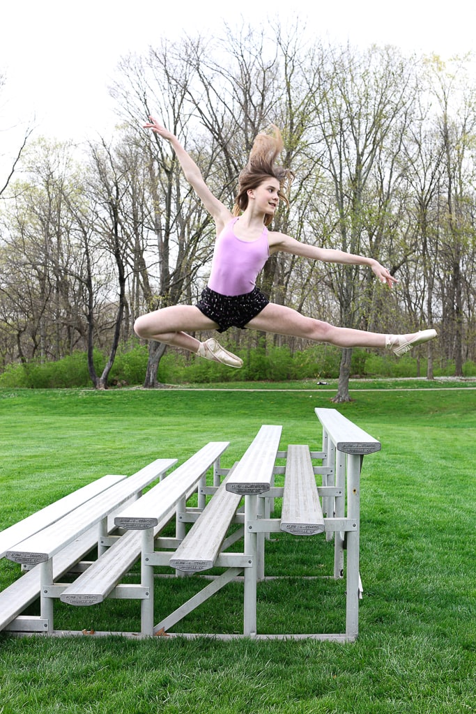 a girl in a flying leap in front of bleachers