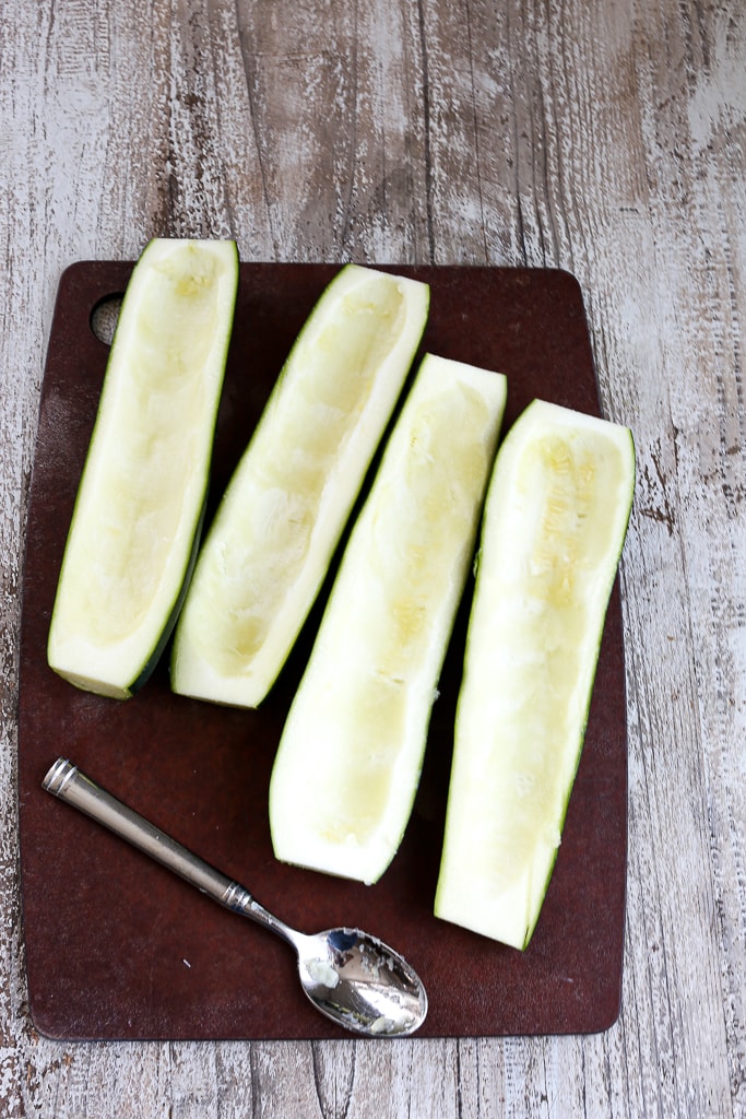 hallow zucchini boats on cutting board with a spoon