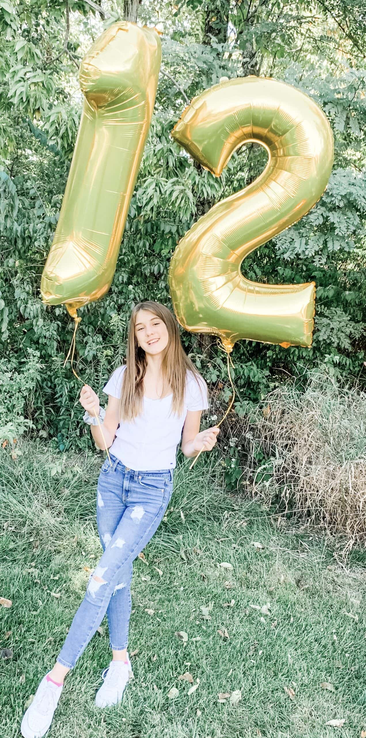 a girl holding two balloons showing the number 12 in gold