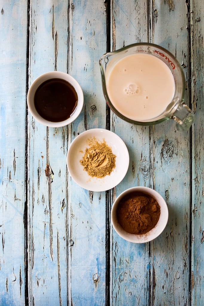 overhead shot of recipe ingredients, almond milk, maca root powder, cocoa powder, and maple syrup