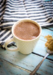 a spoon with maca root powder on it next to a mug of hot cocoa and a black and white striped napkin