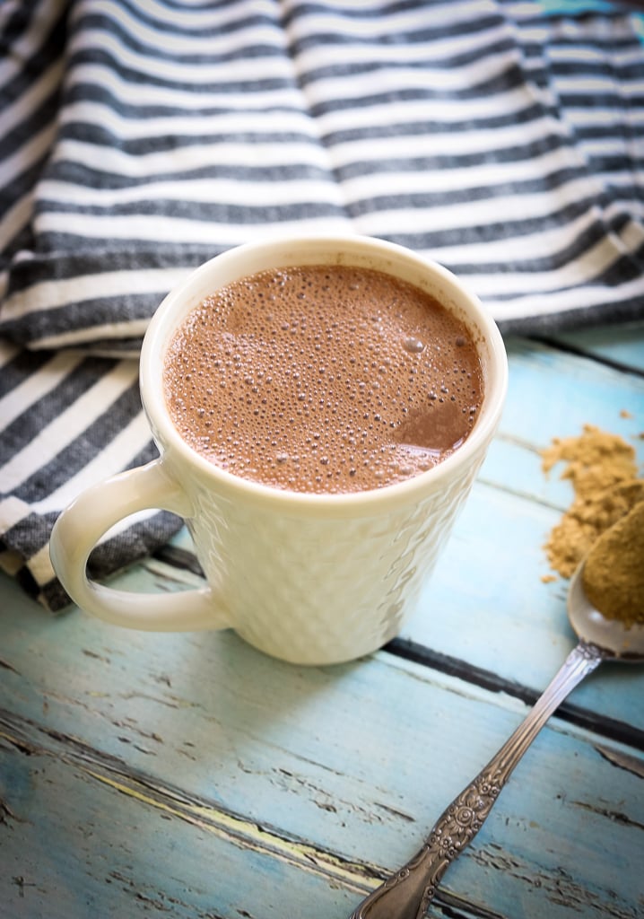 a spoon with maca root powder on it next to a mug of hot cocoa and a black and white striped napkin