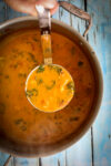 A large soup pot with a ladle of soup being served