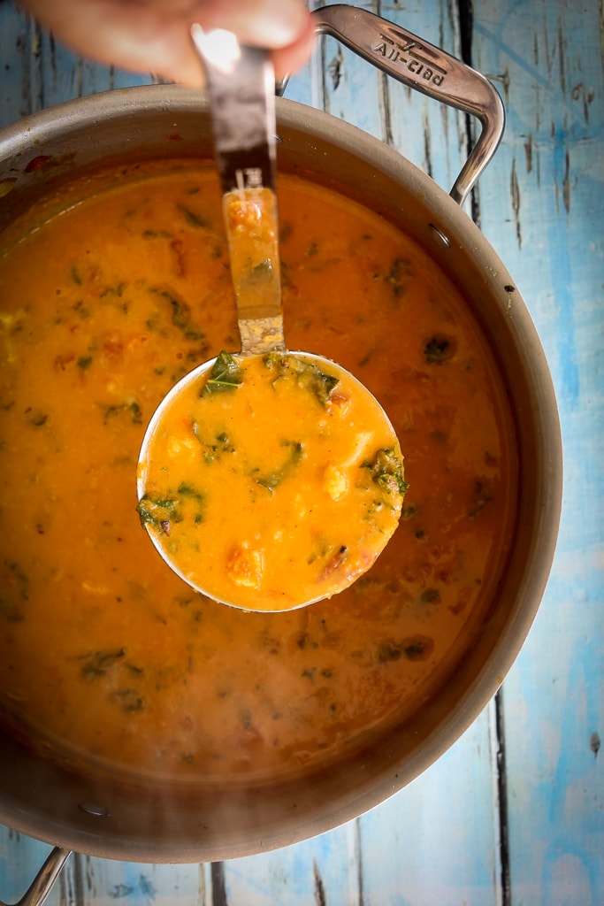 A large soup pot with a ladle of soup being served