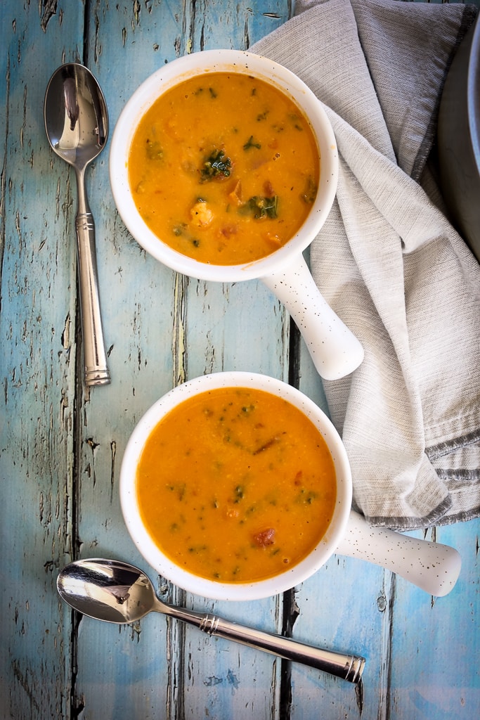 two soup bowls filled with Sweet Potato Soup and two spoons and a napkin