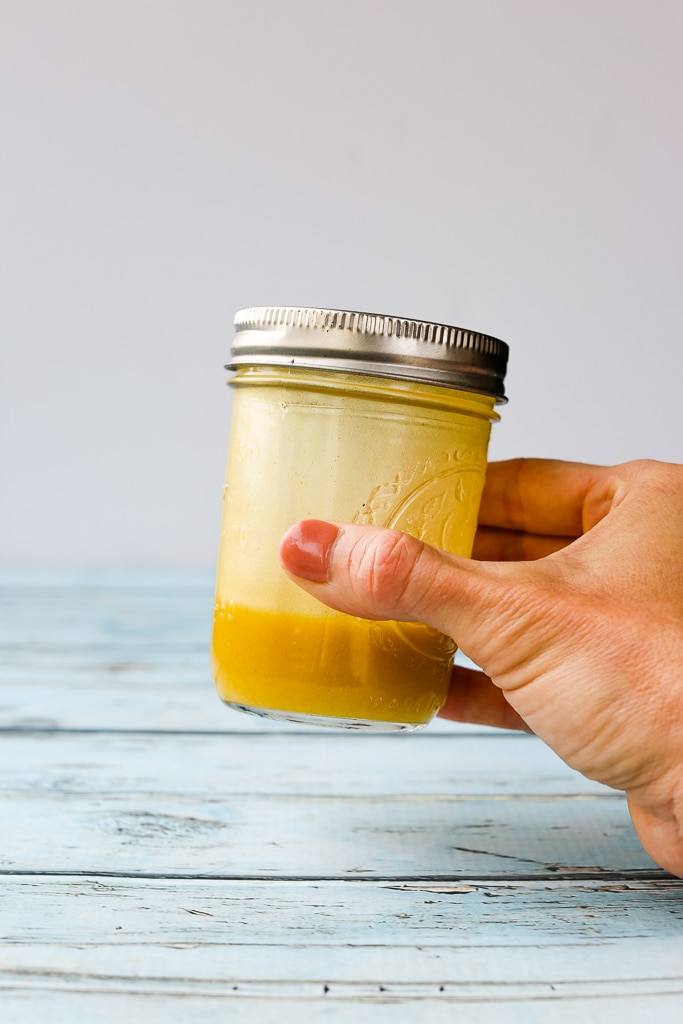 a woman's hand holding a mason jar with a yellow-orange dressing inside