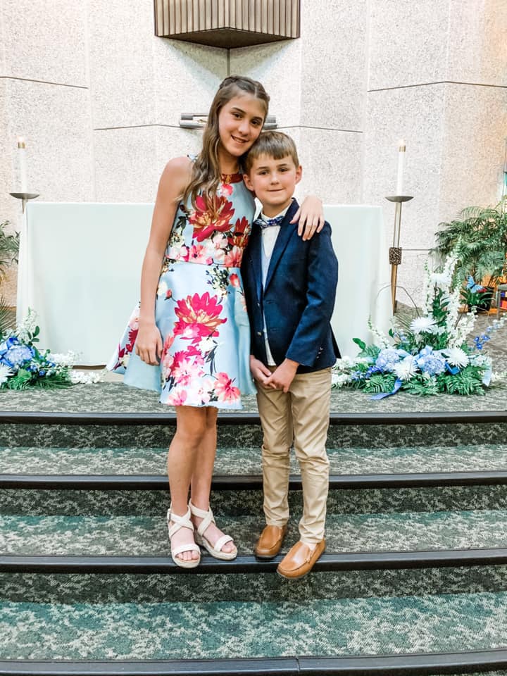 Meghan and Luke in fancy clothes standing on the stairs near the alter in church