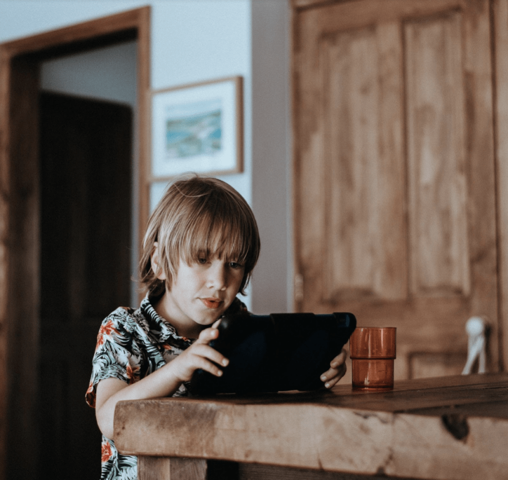 a young boy starting at an ipad screen, sitting at a wooden table
