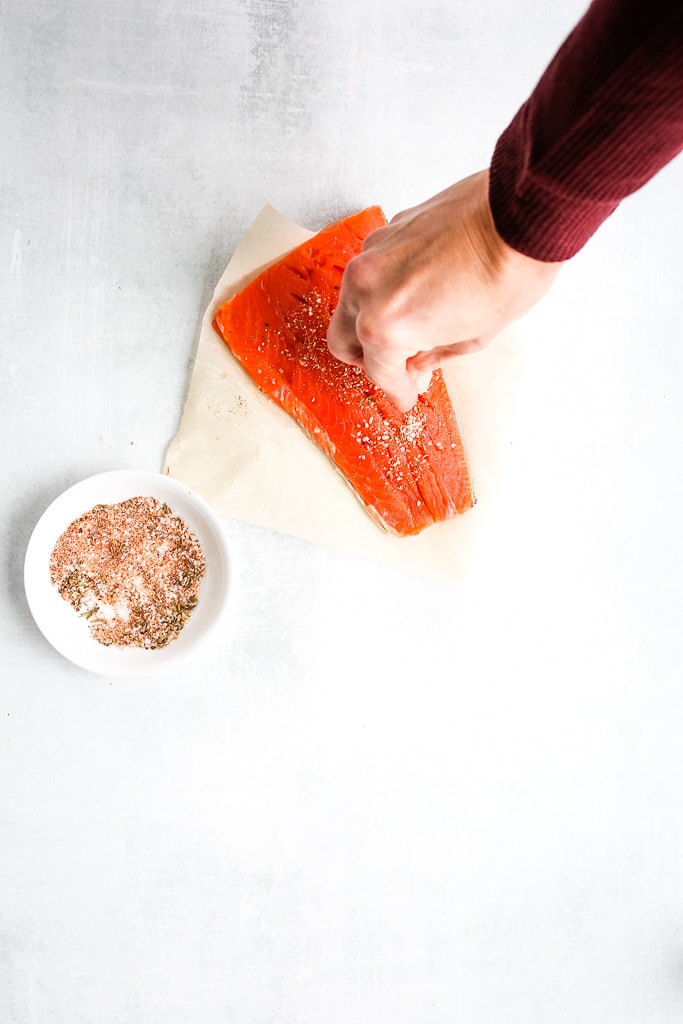 a hand adding seasoning to a raw salmon filet