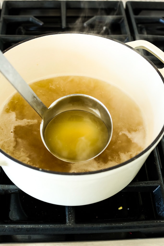 removing a ladle of chicken stock from a pan on the stove
