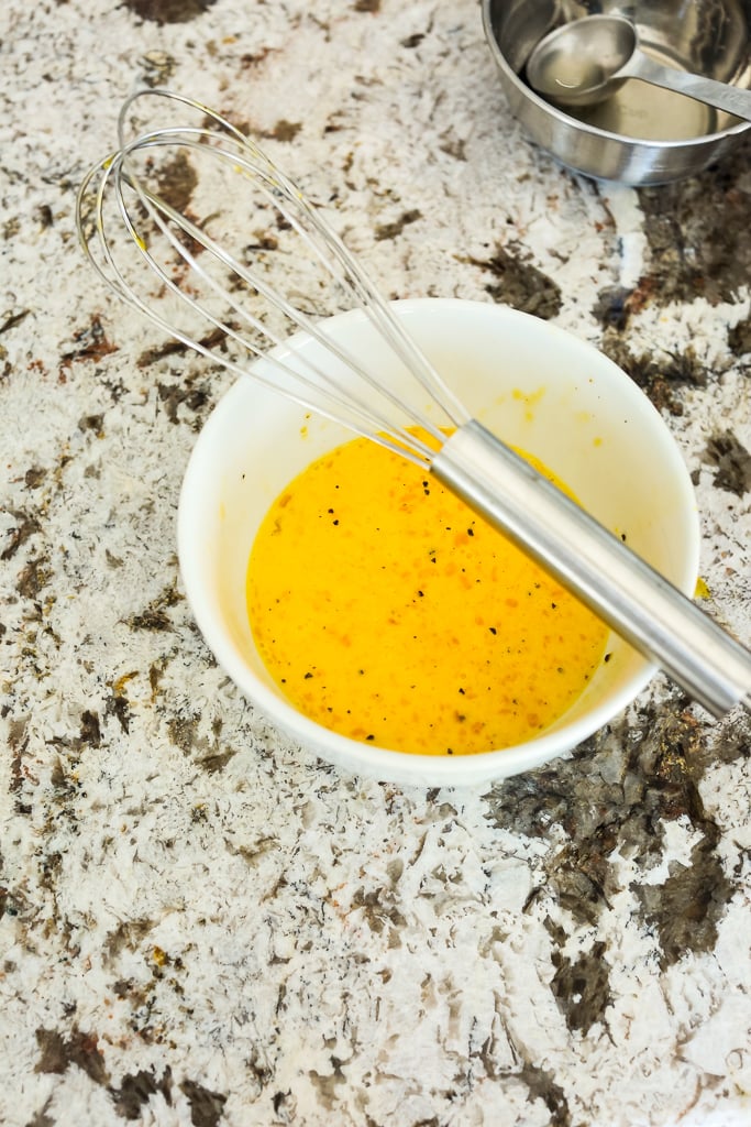 egg mixture in a white bowl with a whisk on top