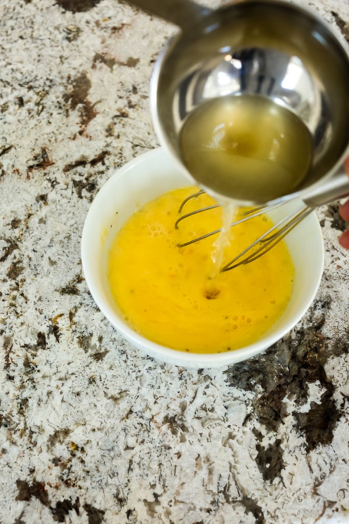 showing how to temper an egg with a ladle of warm broth being stirred into egg mixture
