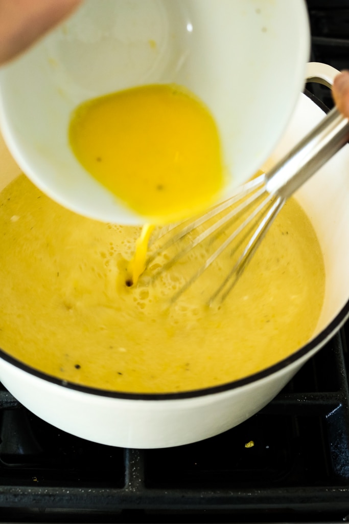 pouring egg mixture into the pot of soup with a whisk
