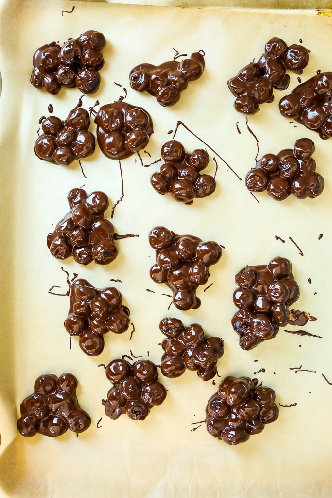 clusters of chocolate covered blueberries on a parchment lined baking sheet