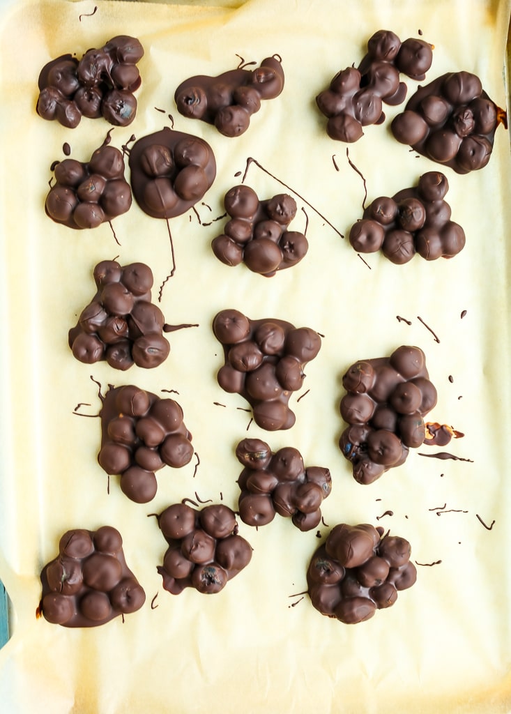 clusters of chocolate covered blueberries on a parchment lined baking sheet