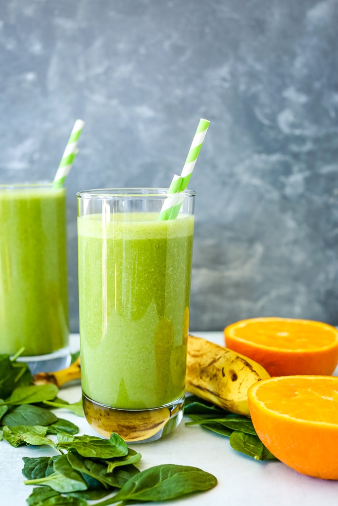 a spinach smoothie with fresh oranges, spinach, and a banana on the table