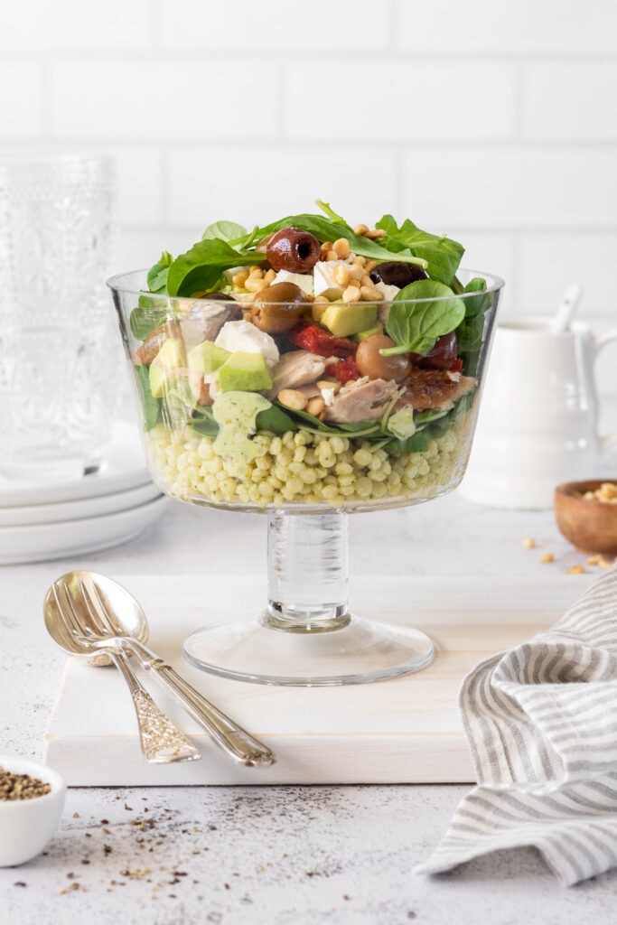 Layered Meditterannean Chicken Salad side view with utensils and plates on the table 