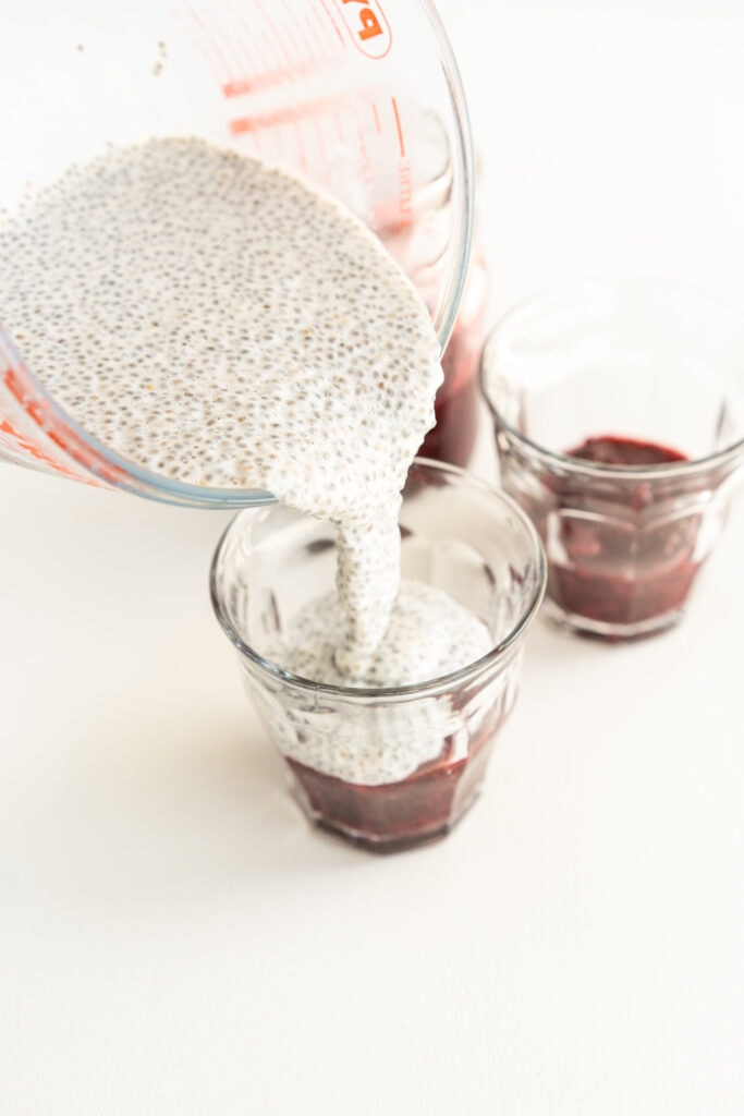 pouring chia pudding into a glass on top of chia jam