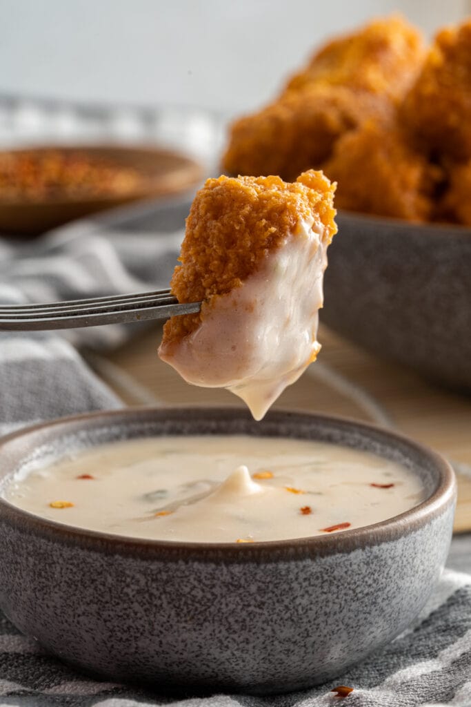 Vegan chicken nuggets--one on a fork dipped in sauce