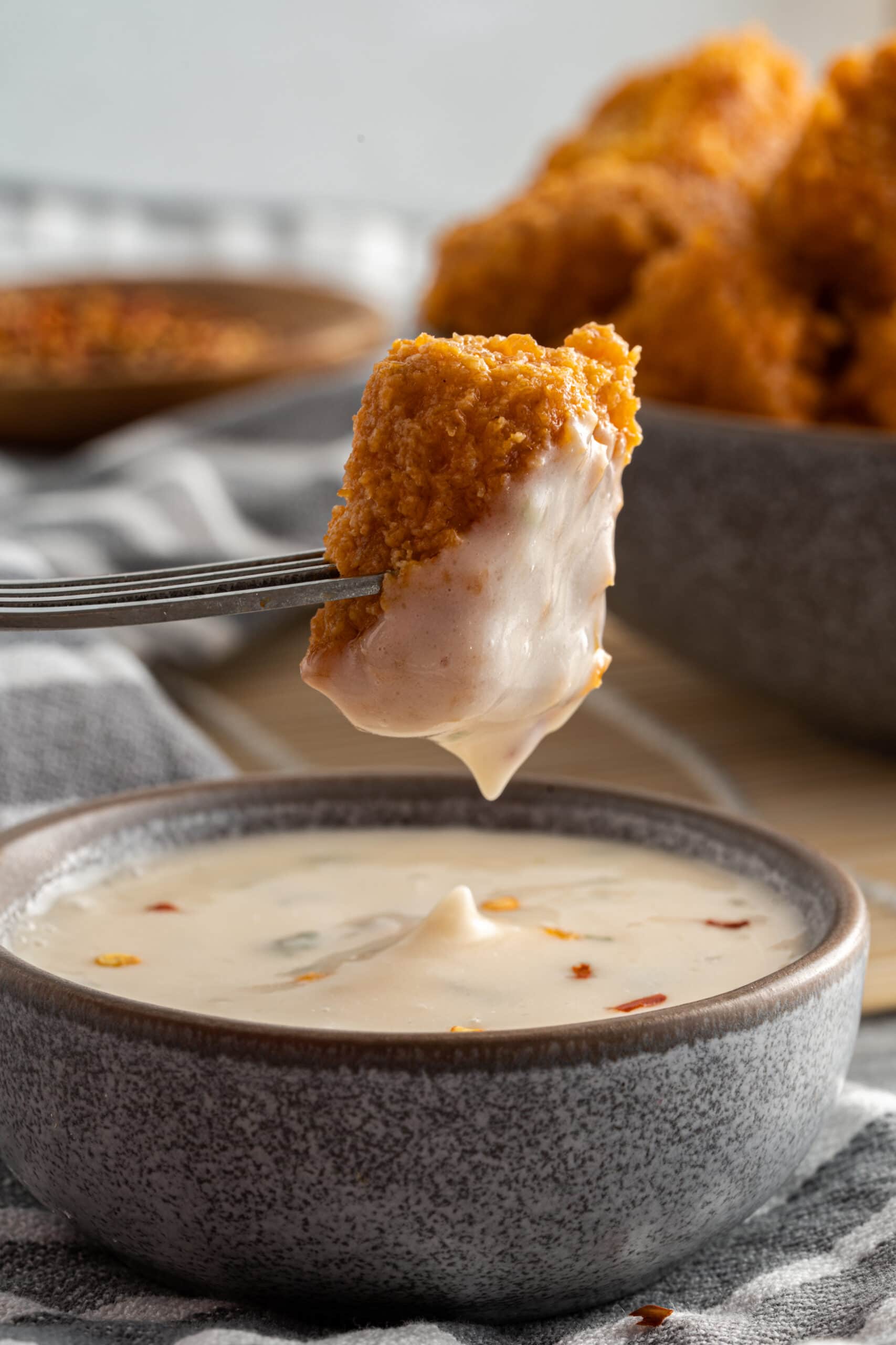 Vegan chicken nuggets--one on a fork dipped in sauce