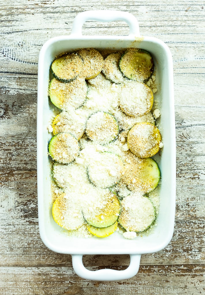 layers of zucchini, summer squash, parmesan cheese, and breadcrumbs in a white baking dish