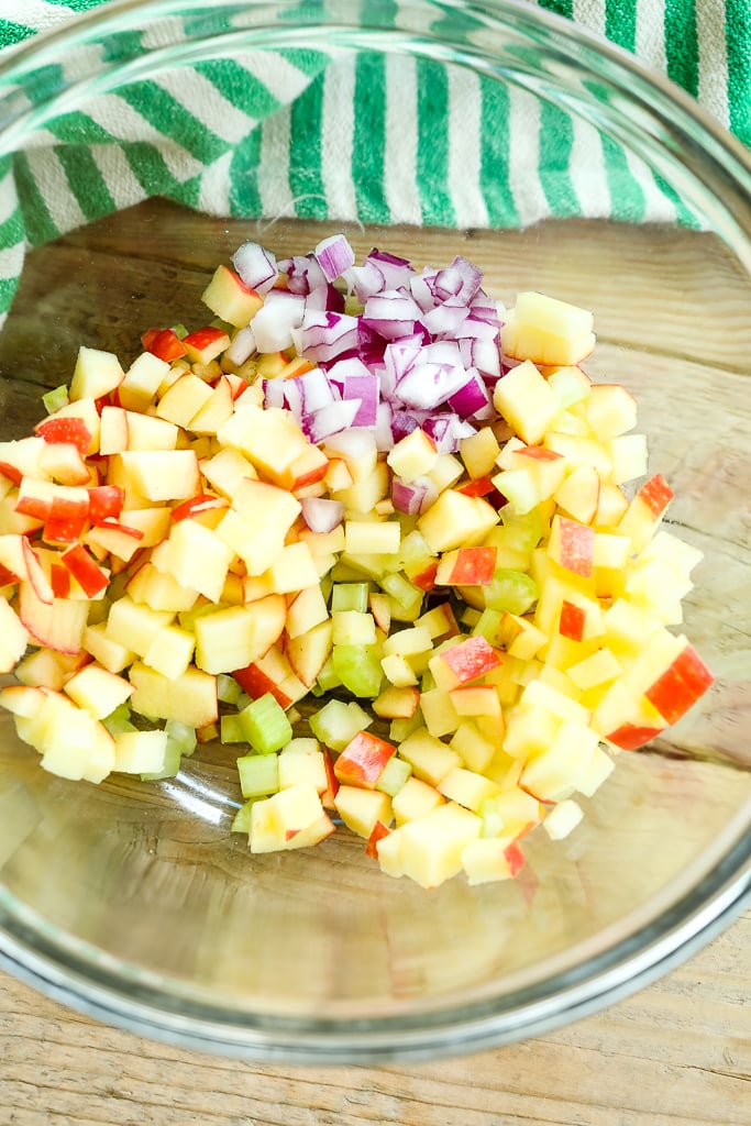a glass bowl with chopped apples, celery, and red onion,