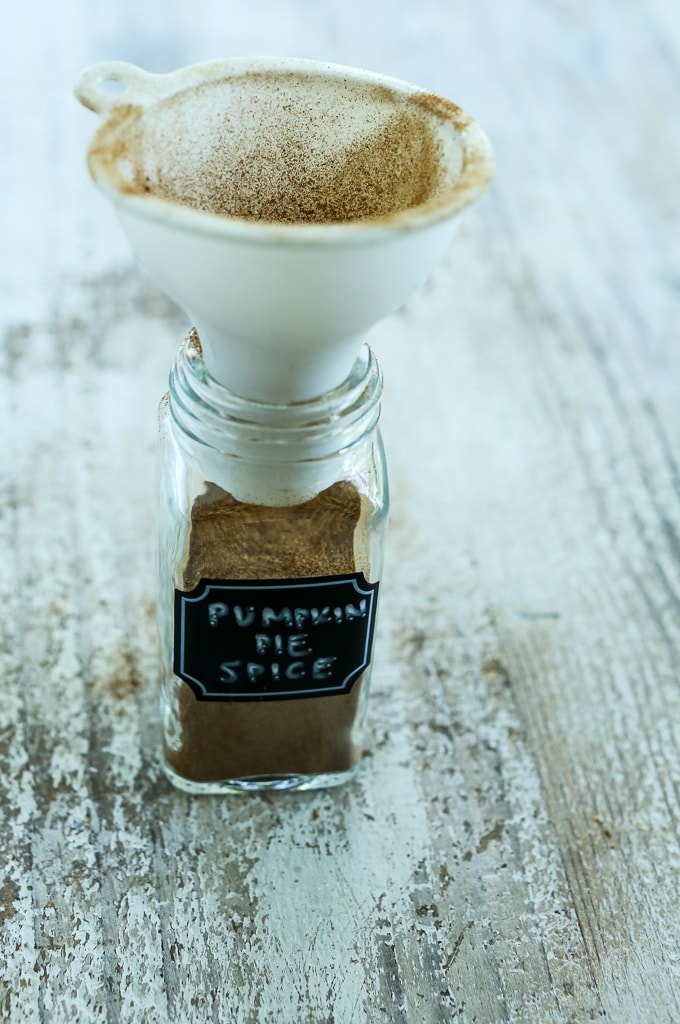 a funnel in a small glass jar with the words Pumpkin Pie Spice " on a label