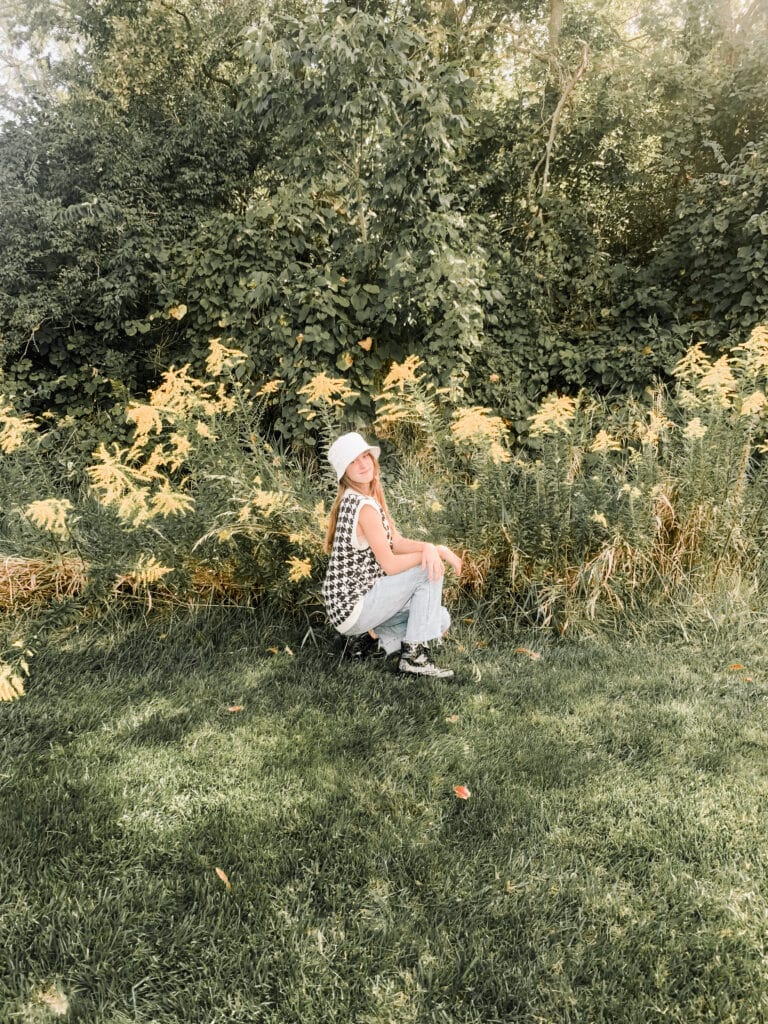 a young girl in jeans squatting in front of yellow flowers