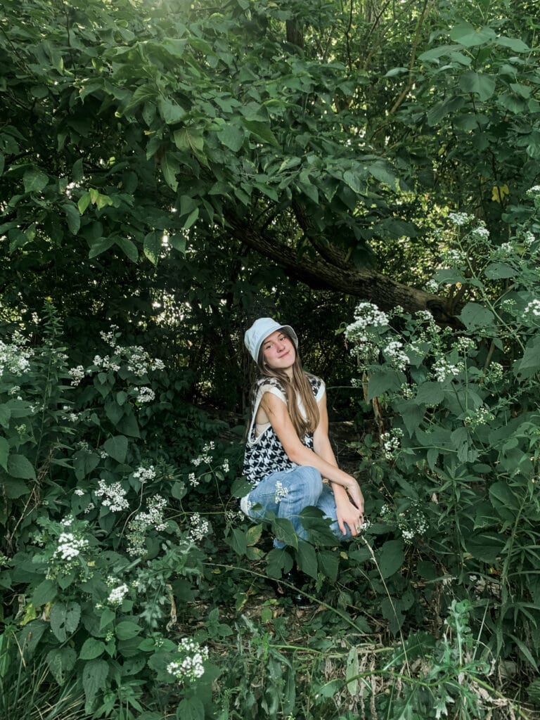 a young girl squatting by some flowers in the woods