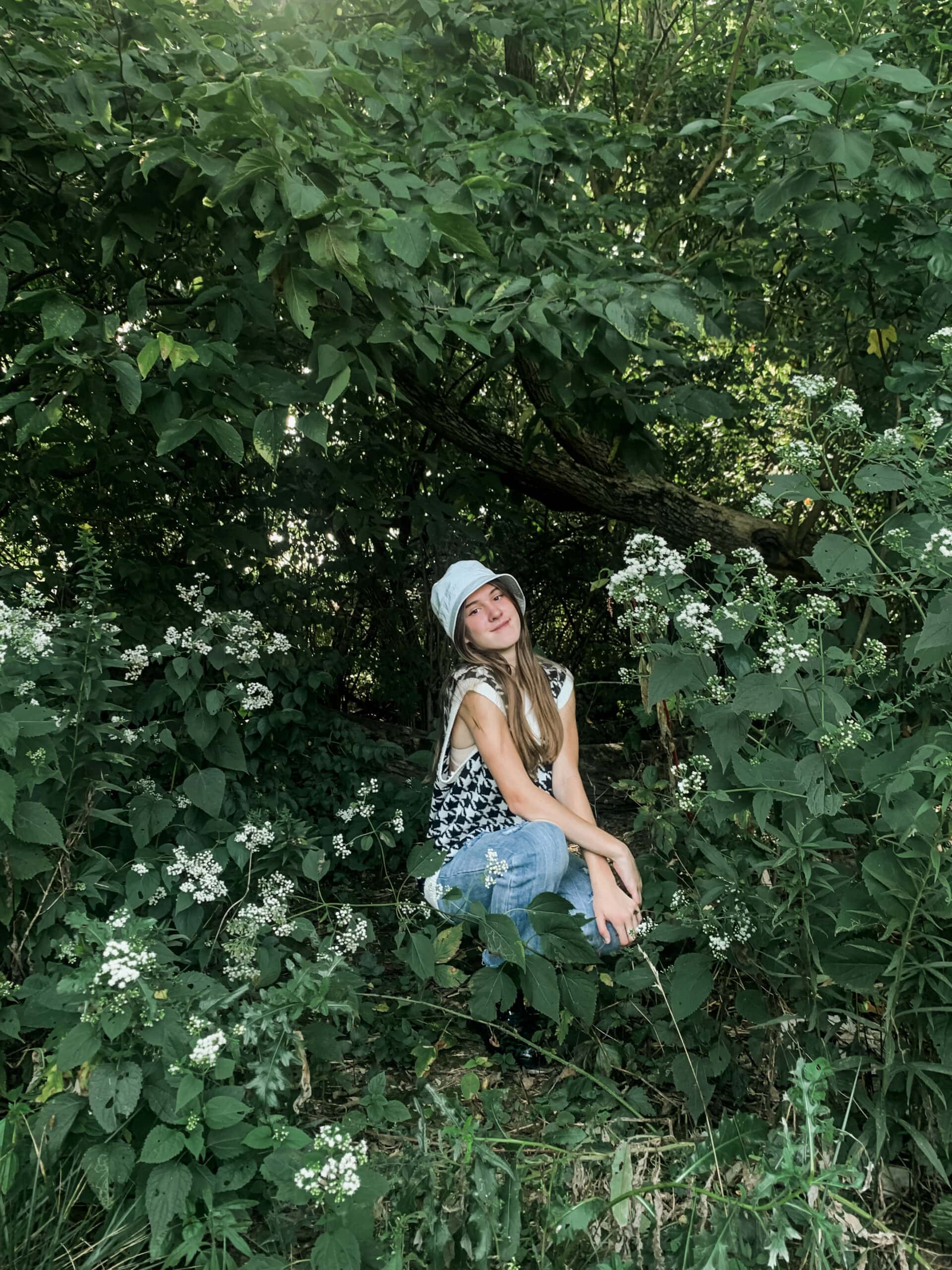 a young girl squatting by some flowers in the woods